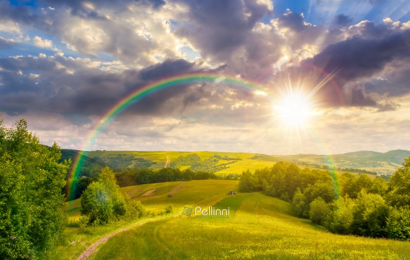 sunset over green mountain field. countryside summertime landsca sunset over green mountain field. countryside summertime landscape with deciduous forest on the grassy hill. cloudy sky with rainbow. nostalgia nature concept. open view for rural life background