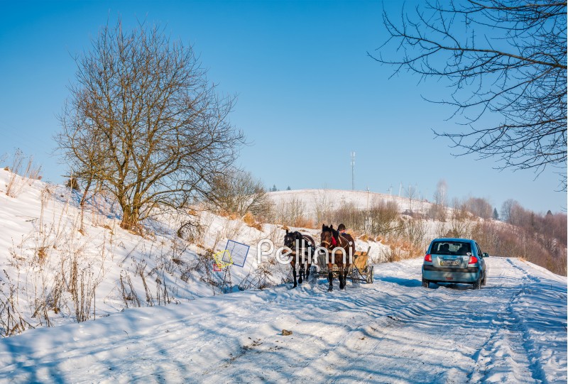 Pilipets, Ukraine - December 21, 2016: traffic in mountainous rural area in winter. cart with two horses and small car pass each other on snowy countryside road
