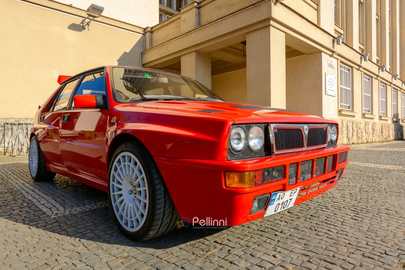 uzhhorod, ukraine - 31 oct 2021: red lancia delta. three quarter front view with grille, headlights and hood of a legendary italian rally car on a cobbled pavement. retro car show on a sunny day