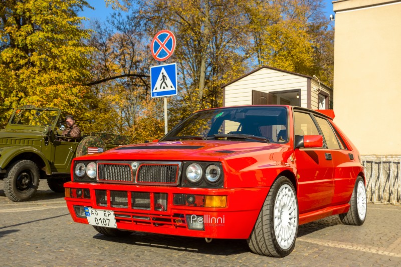 uzhhorod, ukraine - 31 oct 2021: red lancia delta. three quarter front view with grille, headlights and hood of a legendary italian rally car on a cobbled pavement. retro car show on a sunny day