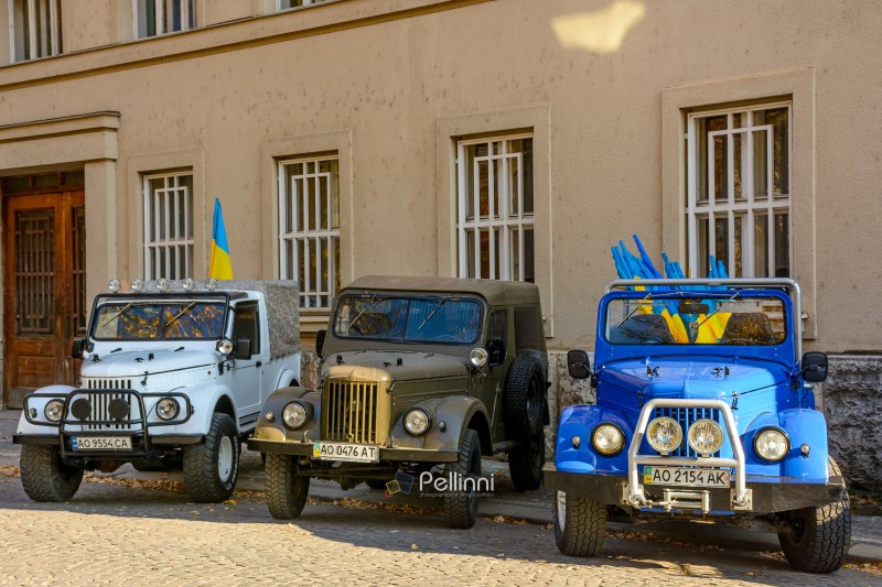 uzhhorod, ukraine - 31 oct 2021: three off road ready oldtimer vehicles. cars with ukrainian flags on a paved road. old military transport modified and tuned for tourism and recreation