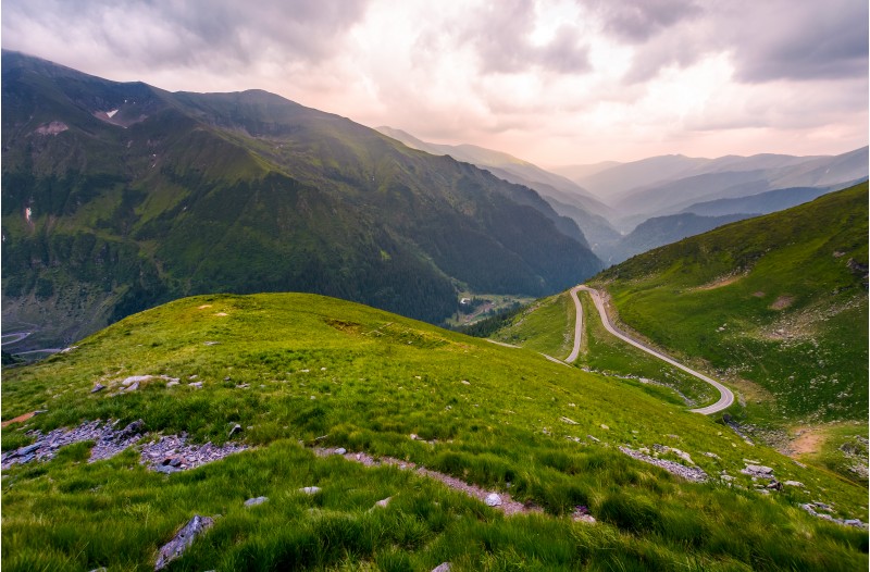 valley in Fagarasan mountains in afternoon. beautiful nature scenery on a cloudy summer day. view from the grassy hillside with footpath. part of Transfagarasan road is visible on the right slope