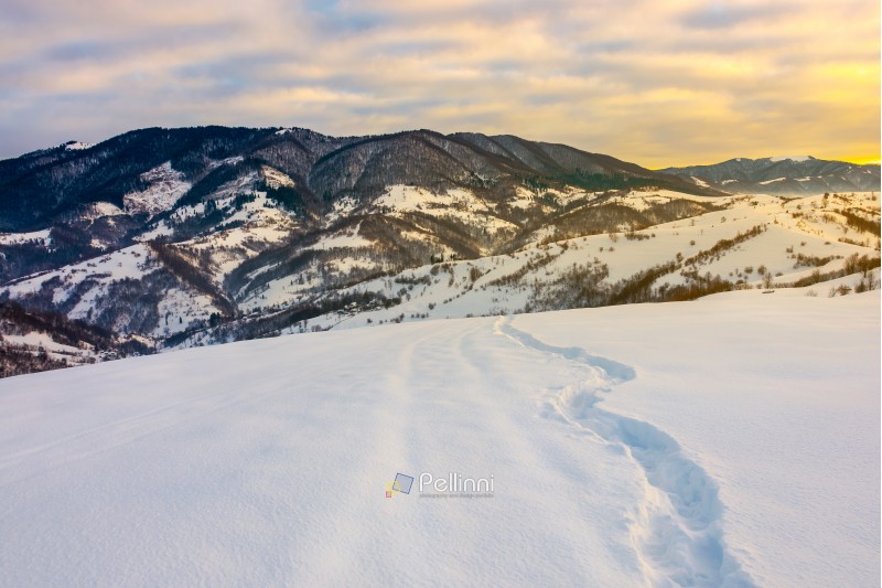 winding foot path through snowy slope in mountains. gorgeous winter landscape at sunrise with cloudy sky