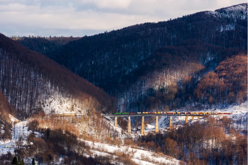 winter rail road transportation in mountains. freight train with colorful carriage on the old viaduct