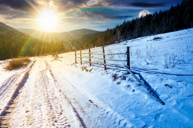 winter solstice in mountainous countryside. day and night time change concept. wooden fence along the road through coniferous forest near snow covered hills. scenic view of scene with sun and moon