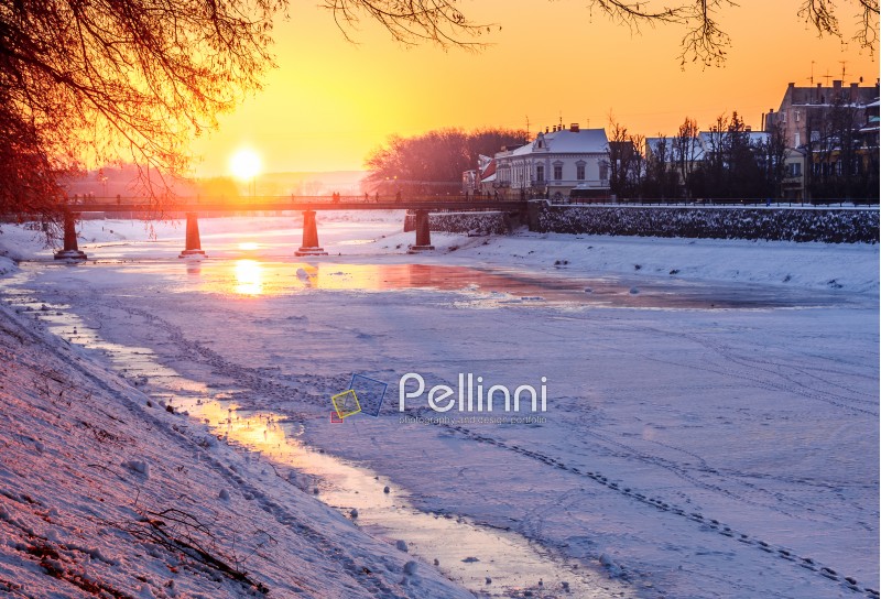 winter sunrise on the bank of ice covered river Uz. Sun over the bridge of old European town Uzhgorod