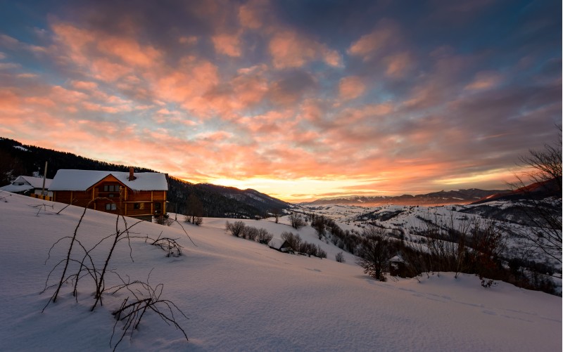 winter sunrise with red clouds in the village. beautiful winter countryside in mountains with snowy slopes