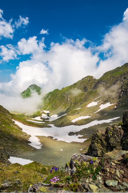 wonderful springtime scenery in mountains. rocky slope with green grass and spots of snow. clouds rising around the distant peak. beautiful sunny weather