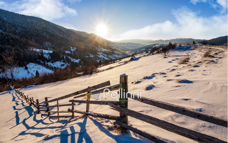 wooden fence in rural area. winter countryside landscape in mountains with snowy fields. beautiful sunny morning