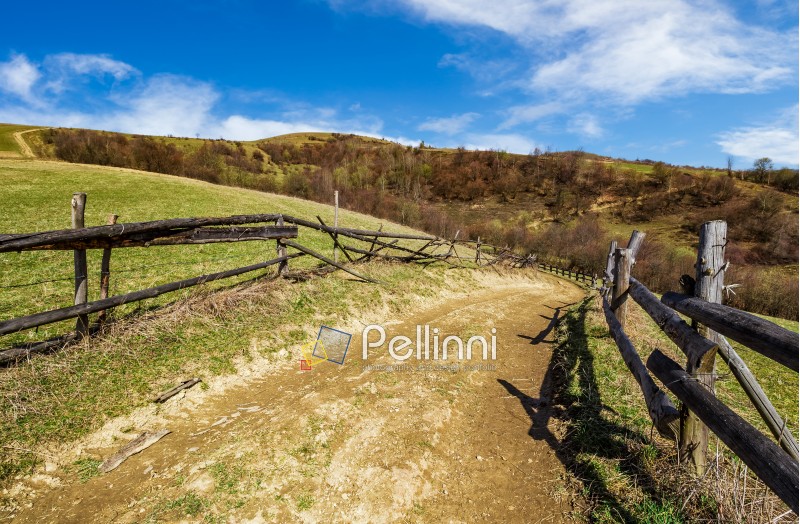 wooden fence by the road in rural area. springtime countryside landscape in mountains with grassy meadows. beautiful sunny weather