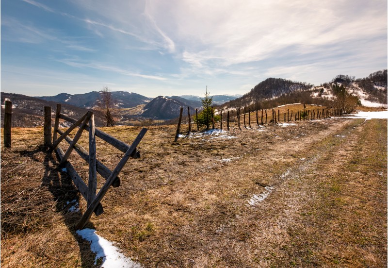wooden fence on a hillside in springtime. beautiful landscape with grassy weathered slopes and some snow in mountains