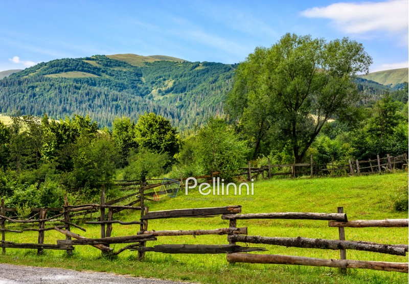 composite image of wooden fence on agricultural grassy meadow with trees on hillside in high mountains