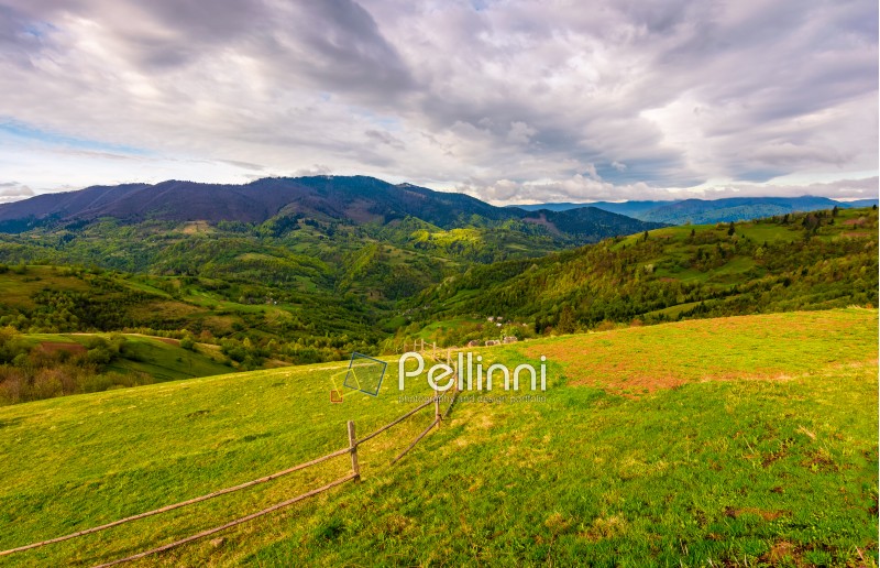 wooden fence on hillside with rural field in mountains. beautiful countryside landscape on cloudy day