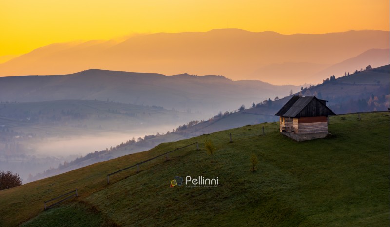 woodshed on a hillside at sunrise. beautiful countryside scenery of mountainous area. yellow sky over the purple mountains. fog down the valley of Synevir village, TransCarpathia, Ukraine