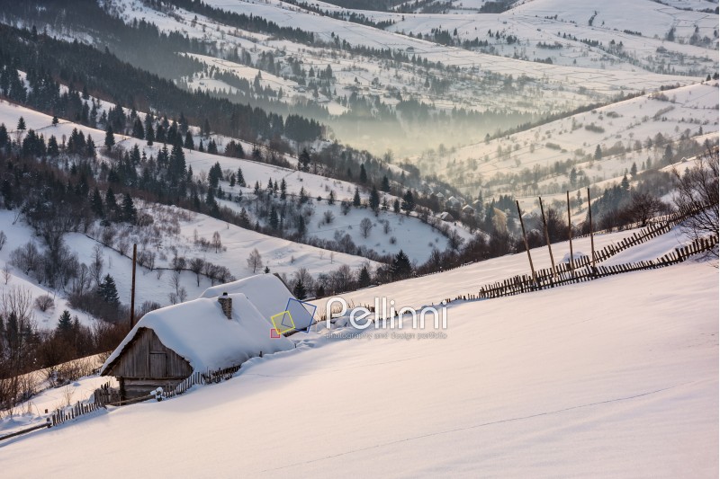 woodshed on hillside in deep snow. beautiful winter rural scenery in the mountainous village outskirts at foggy sunrise