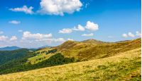 Polonyna Krasna landscape. Ridge of Carpathian Mountains with its peaks, hills, meadows and forests. Blue sky with clouds in late summer day