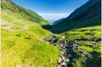 balea stream of fagaras mountains. wonderful serpentine of transfagarasan road on the left side. beautiful summer scenery. power lines along the valley. discover romania