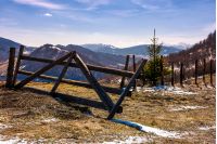 broken wooden fence on hillside. springtime is coming. beautiful mountainous landscape with some snow on slopes with weathered grass on a bright day