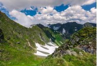 cliffs in the valley of Fagaras mountains. lovely summer scenery on a cloudy day. spots of snow on grassy hillside. beautiful landscape of Romania