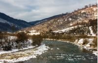 cold flow of river in snowy mountains. ice and snow on the rocky shore. gorgeous winter scenery in rural area on a cloudy day. 