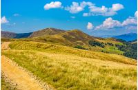 dirt road through alpine hills of mountain ridge. beautiful early autumn landscape in fine weather under blue sky with clouds