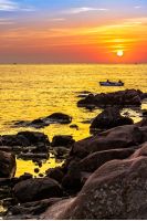 Two fishermen in the boat go fishing at sea in the morning sun near the rocky shore in morning light