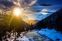 freezing river winding among coniferous forest. day and night time change concept. snow on the ground in countryside valley with sun and moon at twilight. undefined. duality and transition template