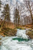 frozen waterfall over the huge boulder on the river among empty forest with old brown foliage on the ground