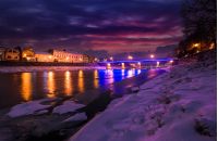 gorgeous evening cityscape of old european town Uzhgorod in winter. beautiful cloudy sky over the river Uzh with some ice and snow on the shore. citylights reflect on the water surface