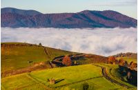 gorgeous morning in mountainous rural area in autumn. wooden fence along the grassy rolling hills with hay stacks fall in to the valley with thick rising fog