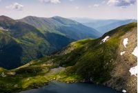 clear lake in mountains with snow and grass on rocky hillside. fine weather in picturesque summer scenery