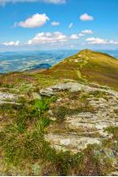 landscape with stones among the grass on the hillside near the path going to mountain top under a blue sky with clouds