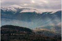 mountain with snowy top over the hill with forest. lovely late autumn scenery with light beams striking through overcast sky