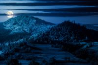 mountainous rural landscape in summer at night. field and forest on the hill in full moon light. alpine countryside in remote region of carpathian mountains