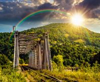 old metal rail road bridge in rural area in mountains at sunset. journey through beautiful landscape in evening light. transportation or retro technology concept. storytelling image under the rainbow