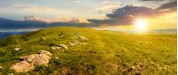 panorama of beautiful carpathian alpine meadows at sunset in evening light. wonderful summer landscape. fluffy clouds on the blue sky. stones on the edge of a hill
