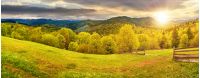 panorama of mountainous countryside in springtime at sunset. beautiful highland landscape. wooden fence on the grassy field. row of trees along the hill. rural area in the distance. cloudy sky