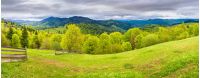panorama of mountainous countryside in springtime. beautiful highland landscape. wooden fence on the grassy field. row of trees along the hill. rural area in the distance. overcast sky