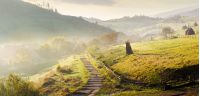 panorama of mountainous rural area on a hazy morning. beautiful landscape of Carpathians. haystacks on the grassy hillside. wooden fence along the footpath