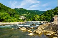 river in forested mountains. beautiful summer landscape with huge rocks on the shore and a white metal train bridge in the distance