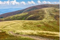 winding road through large meadows on the hillside of mountain range