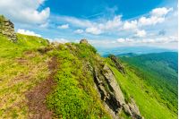 rocky edge of a grassy hillside. mountain ridge in the distance. wonderful summer weather. fleecy clouds on the blue sky