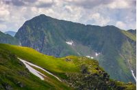 rocky edge on grassy hillside with snow. majestic carpathian summer landscape in romania mountains
