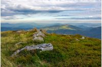 rocky formations on the grassy hills. beautiful mountainous scenery in late summer. colorful grassy carpet on the hillside. forested mountains in the distance in dappled light under cloudy sky