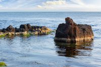 seascape with rock in the water. textured boulder reflecting calm sea surface in morning light. vacation season in summer. sunny weather. fluffy clouds above horizon