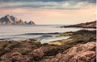 seascape with rocky coast and mountain ridge with high peaks. composite landscape with cloudy sky at menacing sunrise