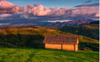 shed on the grassy hillside in red evening light. gorgeous springtime rural landscape in mountains under the blue sky with pink clouds
