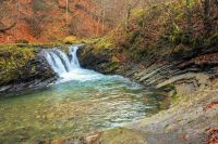 small forest waterfall in autumn. beautiful nature scenery on the river with rocky shore. clear water, fallen foliage and moss on the boulders