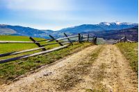 carpathian mountain peaks in snow above green rural meadow near the road with wooden fence