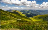 stone among the grass on top of the hillside meadow near the edge of a mountain hill. vivid summer landscape.